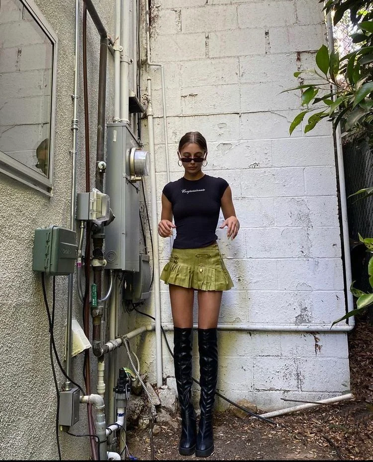 Green pleated mini skirt with black top and over-the-knee boots