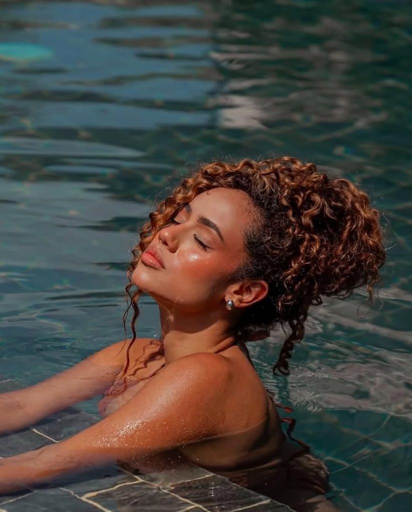 Woman with curly hair in a pool, relaxed, sun-kissed, natural beauty, spring hairstyle.