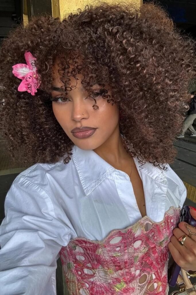 Elegant curly hairstyle with floral accessory, sophisticated, spring elegance.