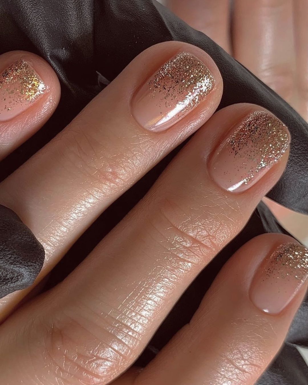 Nude nails with gold glitter accents.