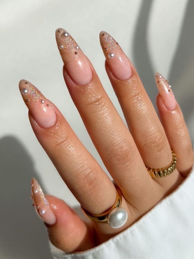 Long almond-shaped nails with glitter and pearl-studded tips, embodying glamorous and elegant nail art trends.