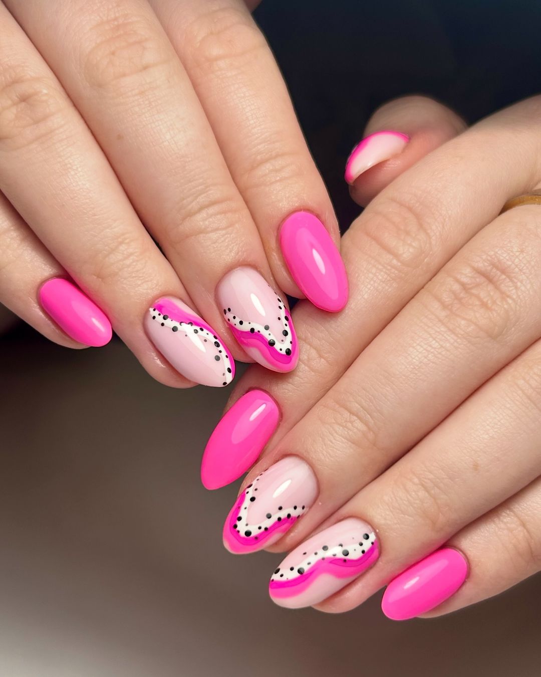 Pink wave nails with dot accents on almond shape.
