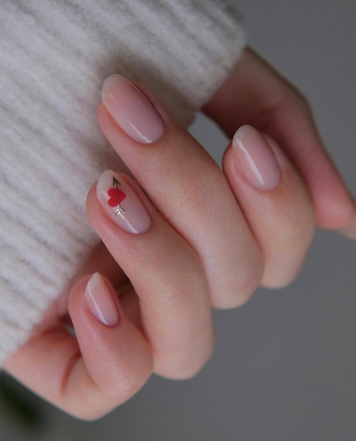 Nude nails with delicate red arrow design, short almond shape