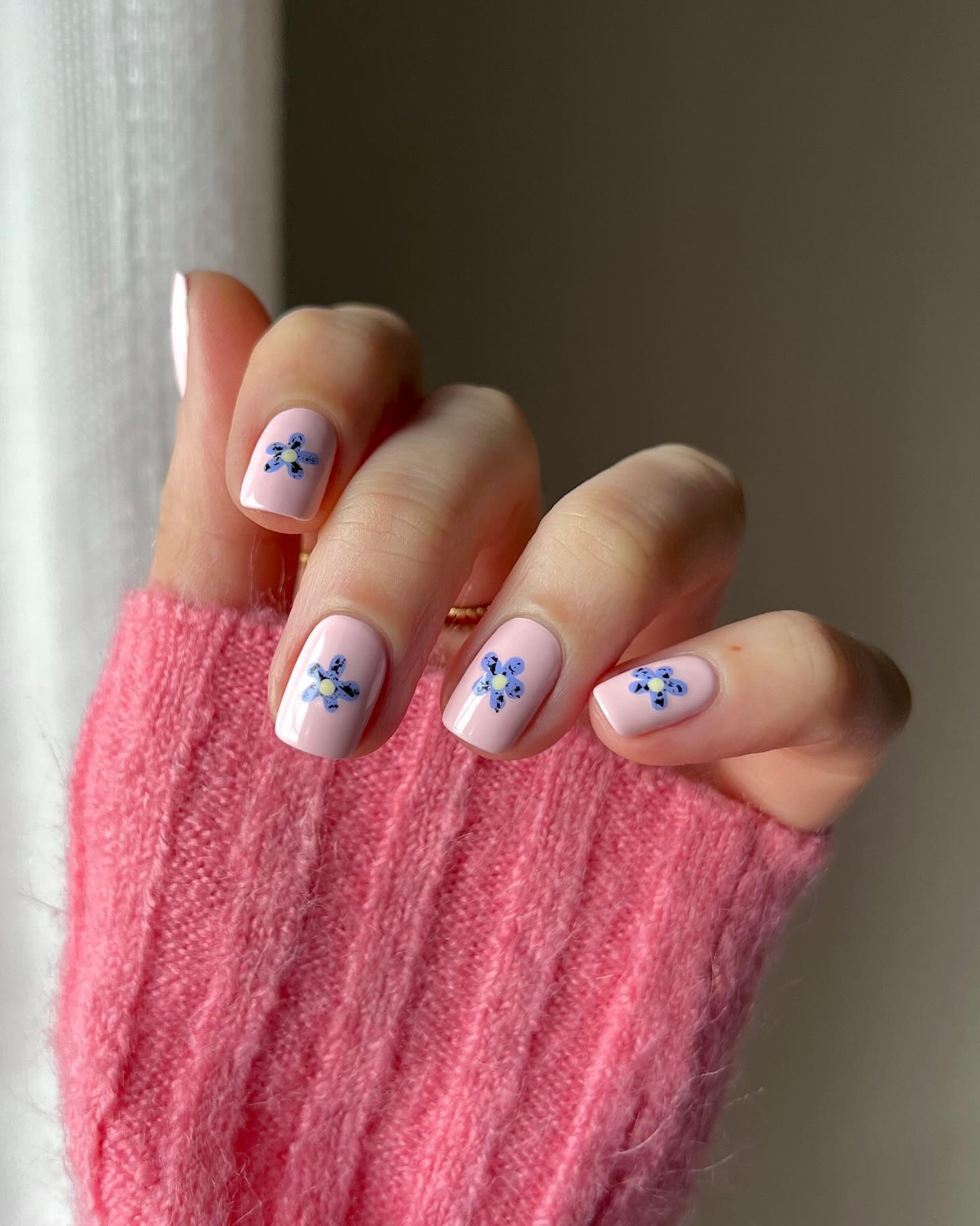 Short square nails with blue floral nail art on pink base