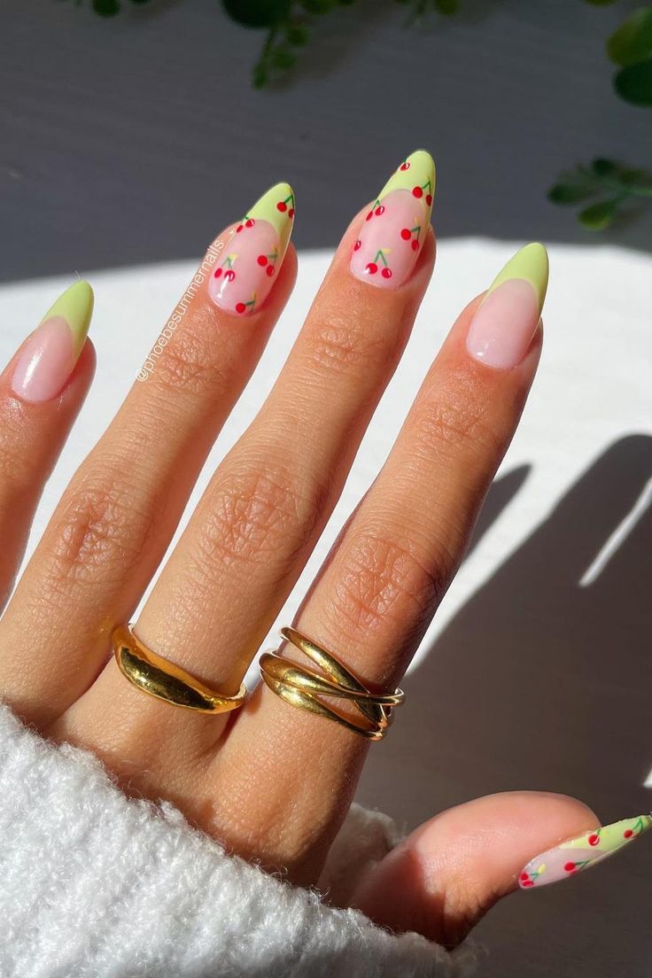 Green and pink French tips with cherry motifs on almond nails.